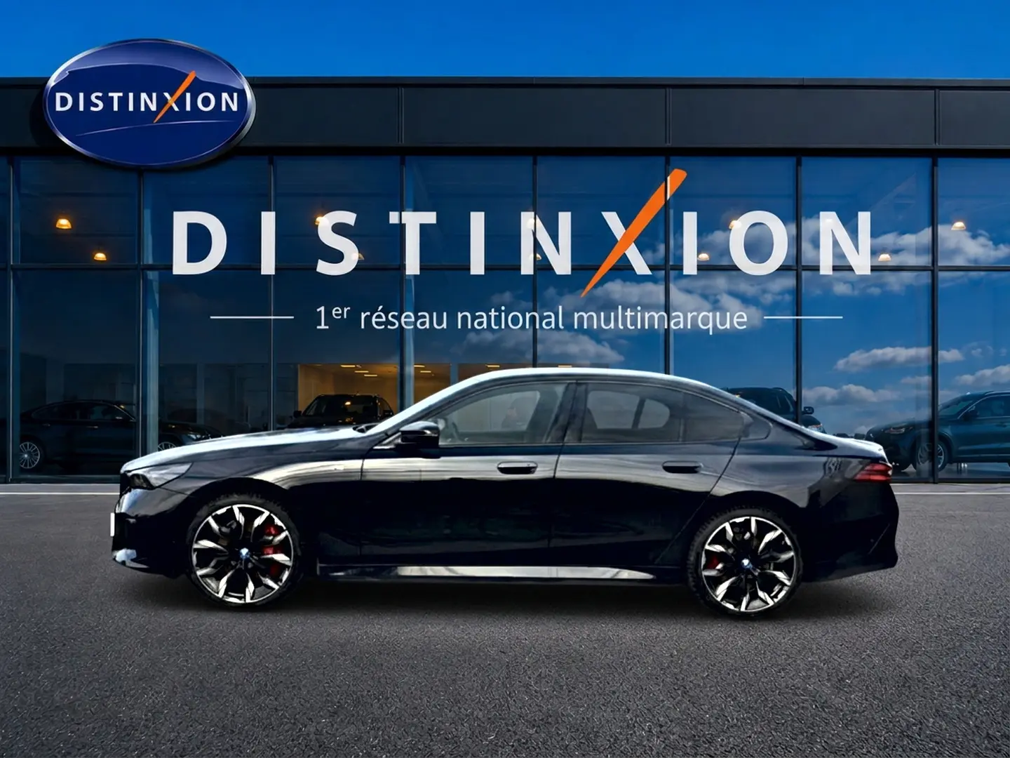 Profil latéral gauche d'une BMW Série 5 i5 M60 noire avec jantes alu bicolores devant un showroom Distinxion.
