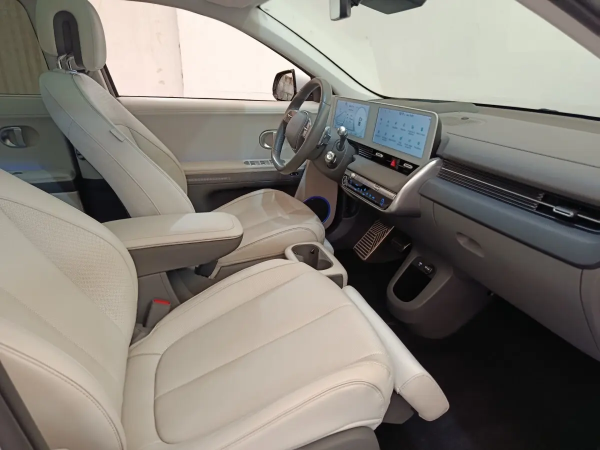 Vue intérieure côté conducteur de la Hyundai IONIQ BEV 77KWH AWD Executive 2023 avec sièges beige et tableau de bord numérique.