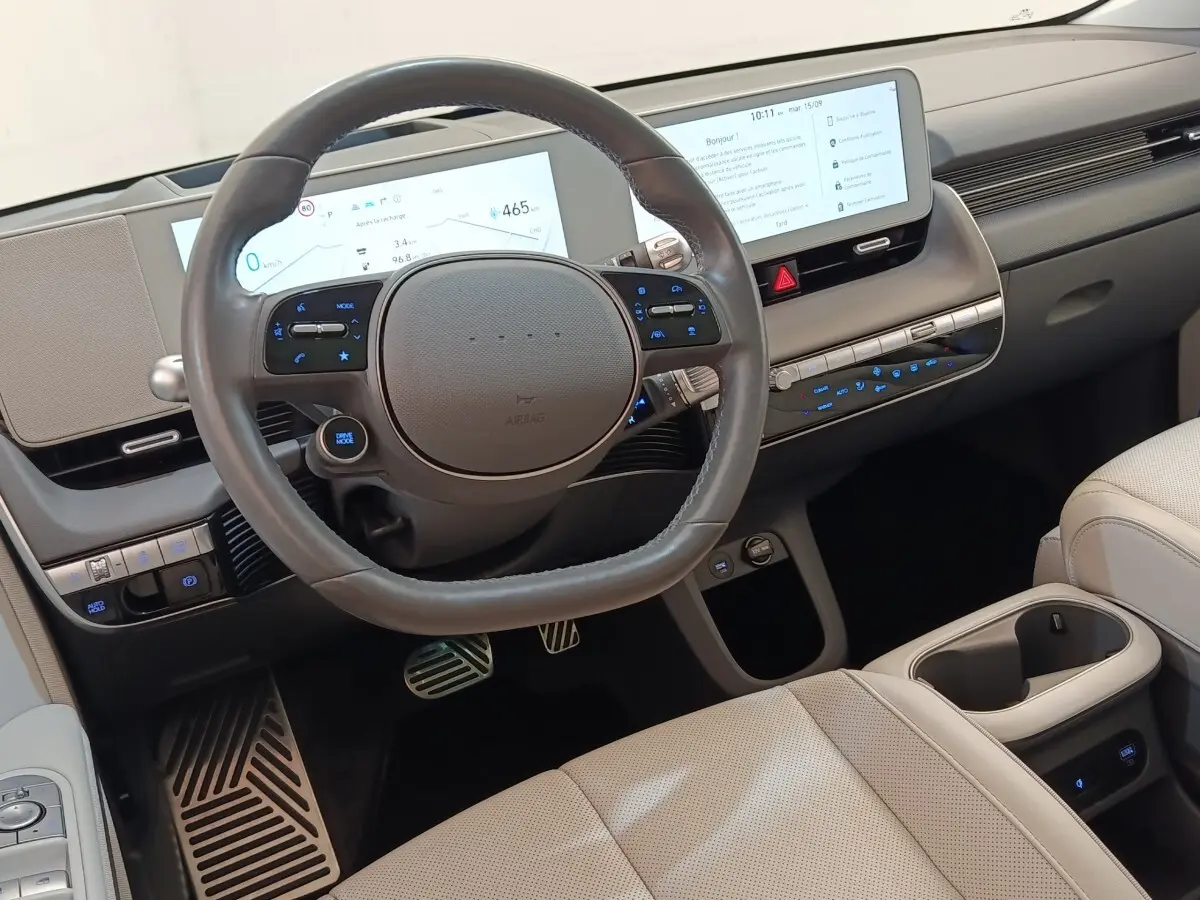 Vue intérieure centrée sur le volant cuir et tableau de bord numérique de la Hyundai IONIQ BEV beige 2023.