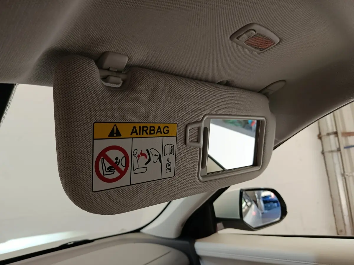 Détail intérieur du pare-soleil côté conducteur beige avec miroir et avertissement airbag, rétroviseur extérieur visible.