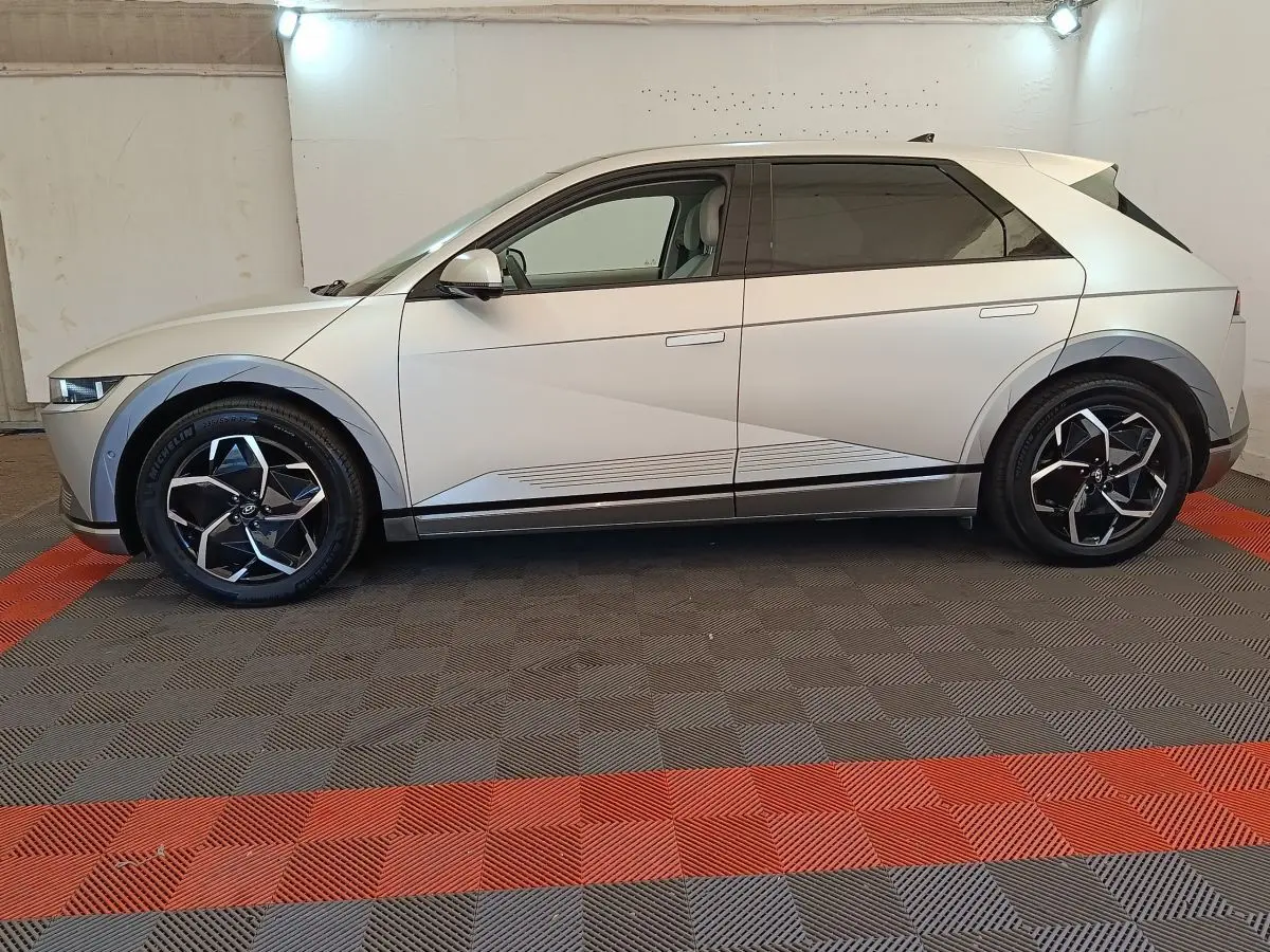 Vue de profil côté gauche d'une Hyundai IONIQ électrique beige 2023 avec jantes noires et détails géométriques sur la carrosserie.