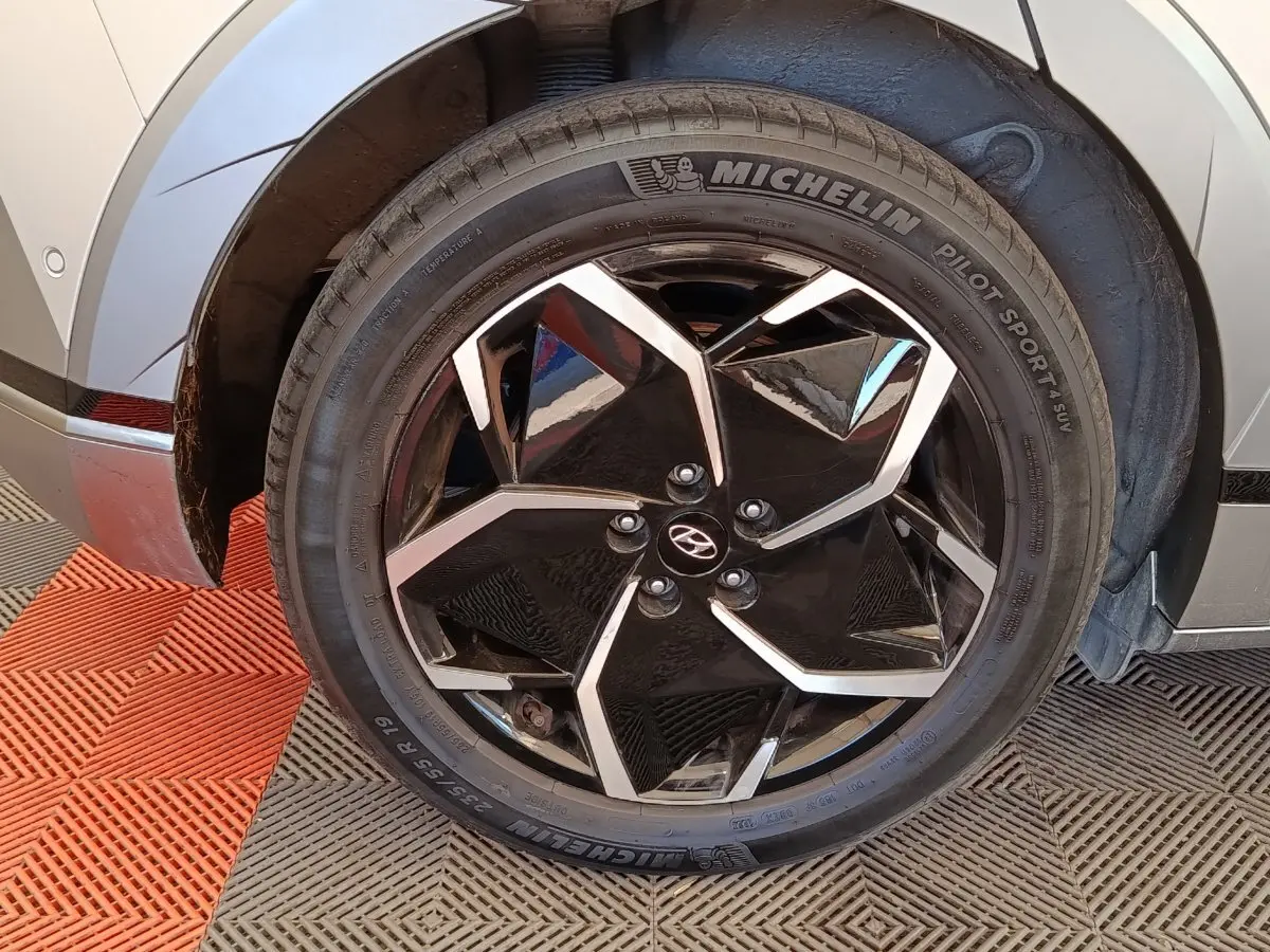 Gros plan sur la roue avant droite avec jante noire et argentée du Hyundai IONIQ beige 2023 électrique.