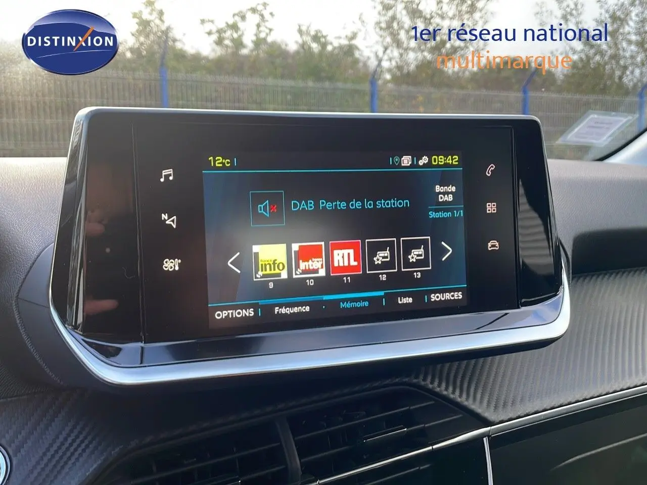 Écran tactile central du tableau de bord de la Peugeot 208 électrique gris Artense, affichant les stations radio numériques.