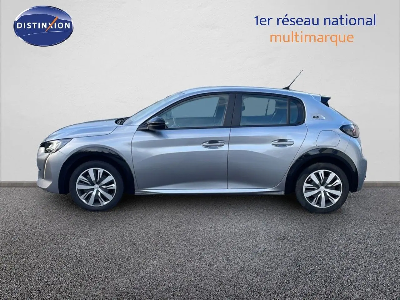 Profil côté gauche d'une Peugeot 208 électrique gris artense, version Active Business, garée devant un mur blanc.