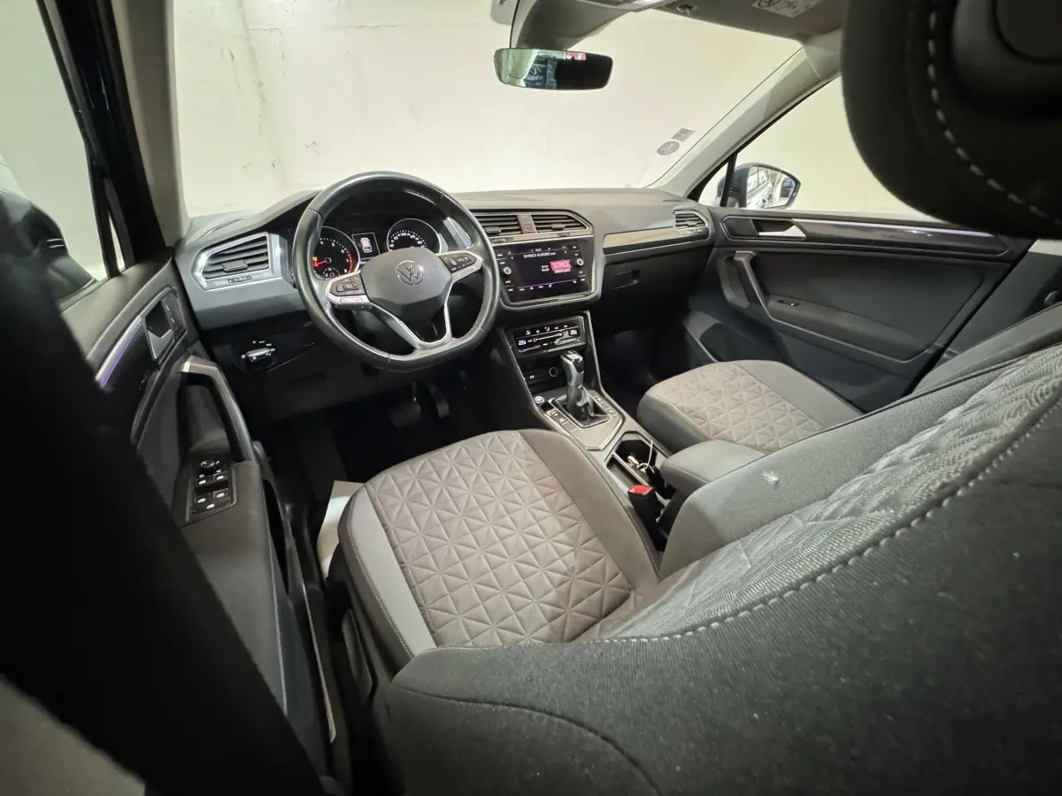 Vue intérieure avant du Volkswagen Tiguan 2021, sièges gris à motifs, volant cuir multifonctions et écran tactile central.