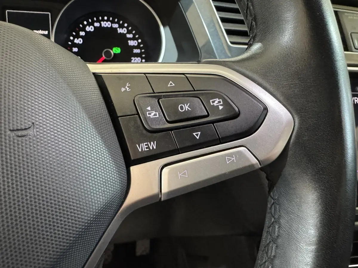 Gros plan sur les commandes multifonctions à droite du volant cuir noir du Volkswagen Tiguan bleu, tableau de bord en arrière-plan.