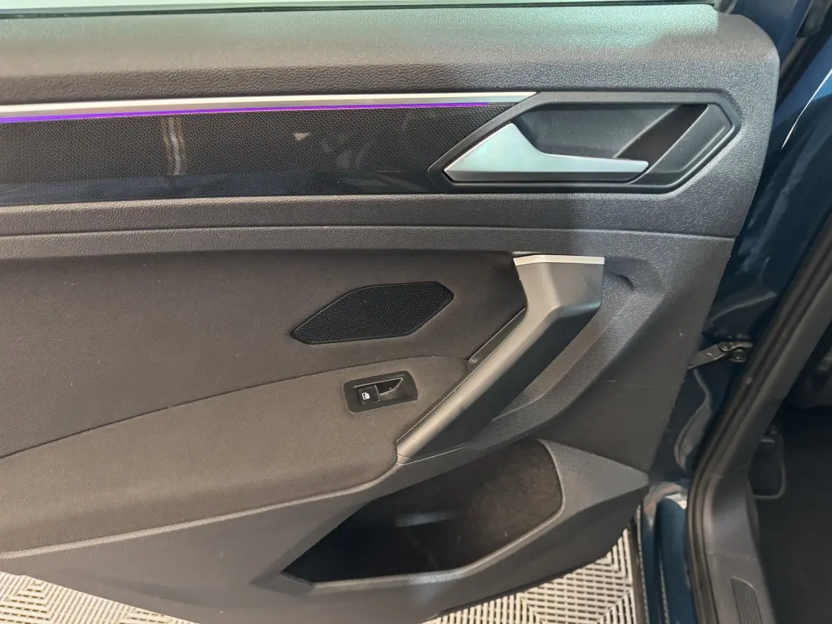 Détail de la porte arrière gauche du Volkswagen Tiguan bleu, avec éclairage d’ambiance violet et poignée argentée.