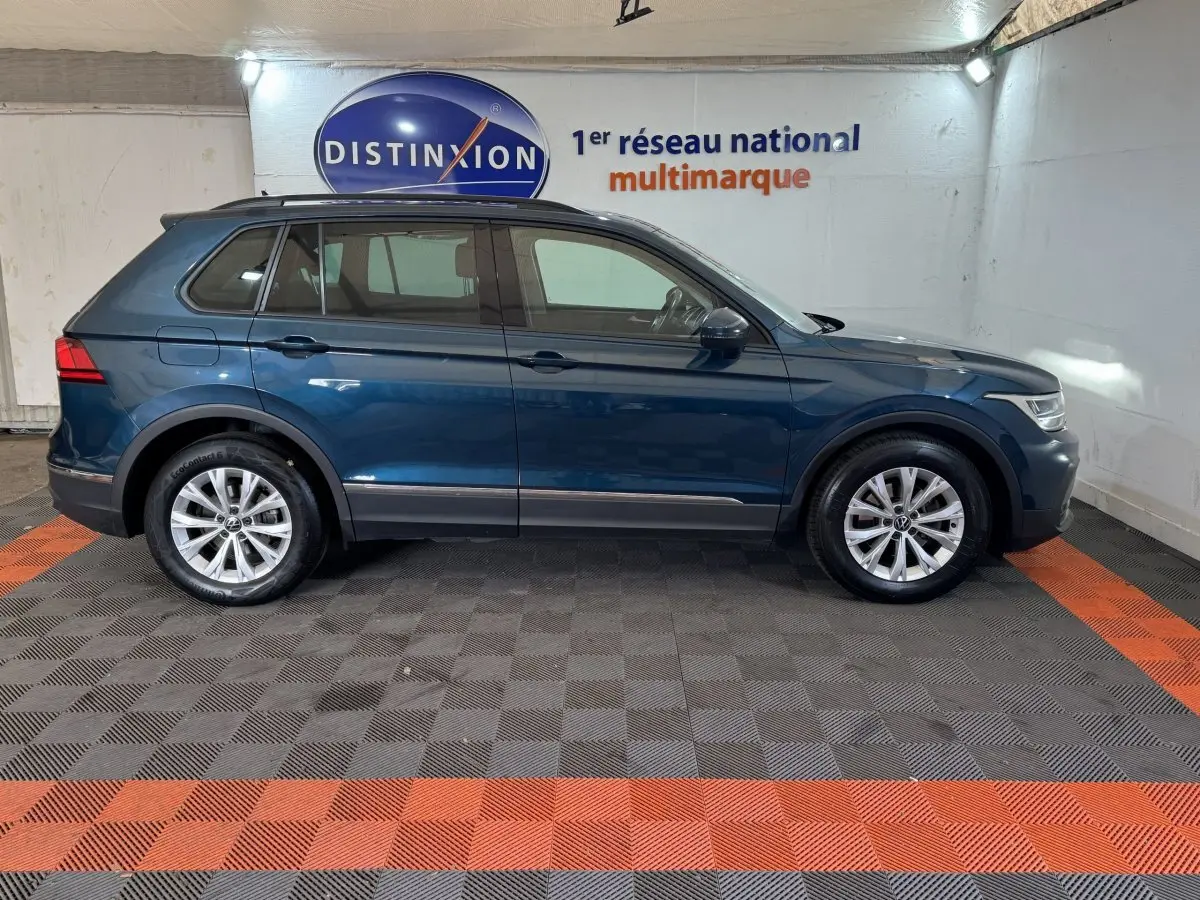Vue latérale droite d'un Volkswagen Tiguan bleu 2021 avec rails de toit noirs dans un showroom.