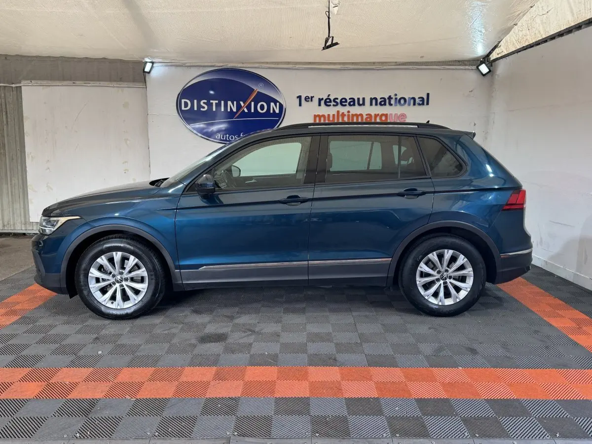 Vue de profil côté gauche d'un Volkswagen Tiguan bleu avec rails de toit noirs dans un showroom.