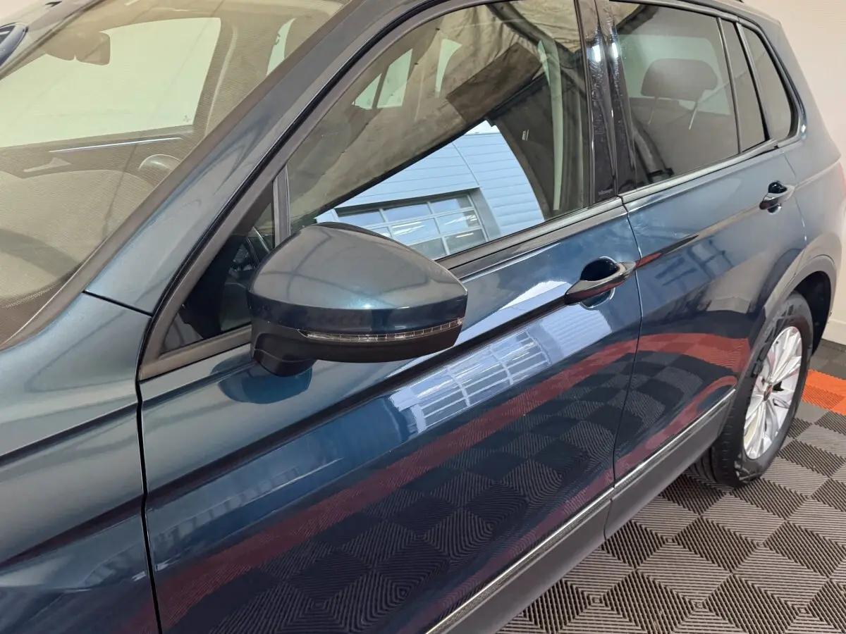 Vue latérale côté gauche du Volkswagen Tiguan bleu avec rétroviseur noir et jante visible sur sol damier.