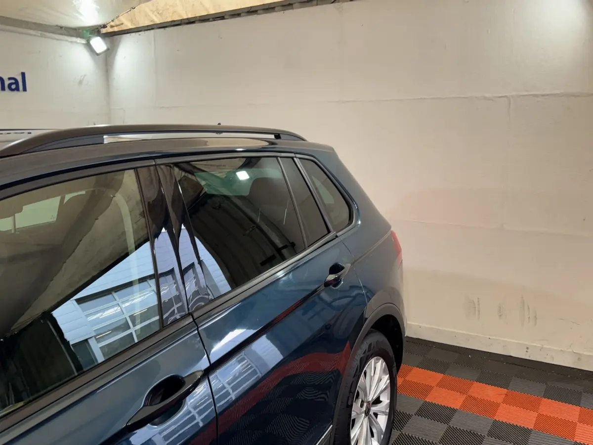 Vue 3/4 arrière droite du Volkswagen Tiguan bleu avec rails de toit noirs dans un garage.