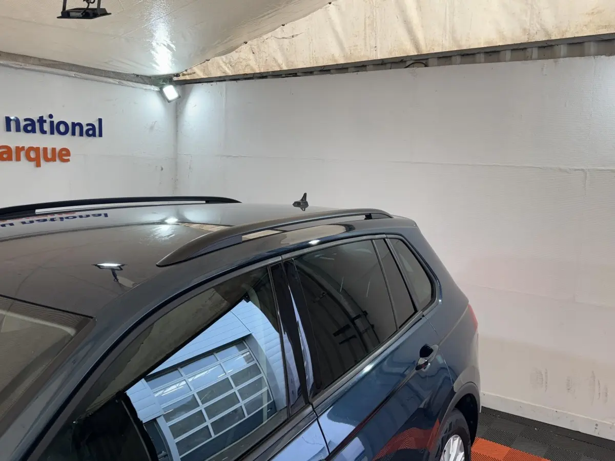 Vue latérale droite d’un Volkswagen Tiguan bleu avec rails de toit noirs dans un garage éclairé.