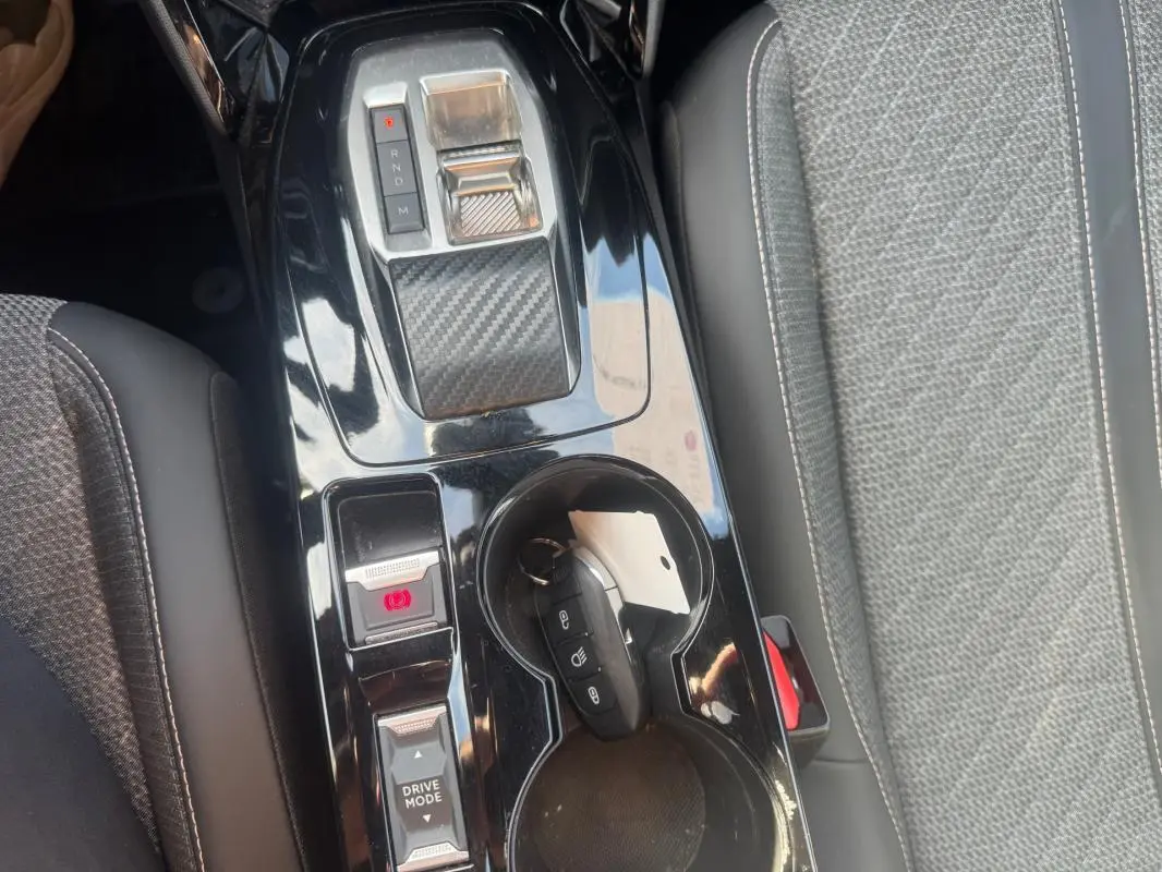 Vue rapprochée de la console centrale noire brillante du Peugeot 2008 Hybrid 145 avec sélecteur de vitesse et porte-gobelets.