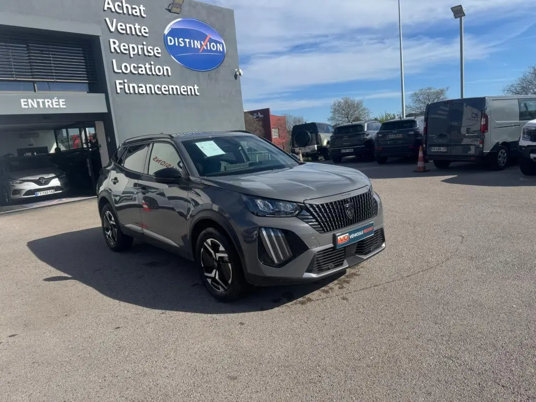 Peugeot 2008 Hybrid 145 gris en 3/4 avant droit, jantes alliage 17 pouces, devant un concessionnaire Distinxion.