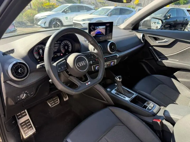 Vue intérieure côté conducteur de l'Audi Q2 35 TDI S line 2025, avec volant sport, écran central et finitions noires.
