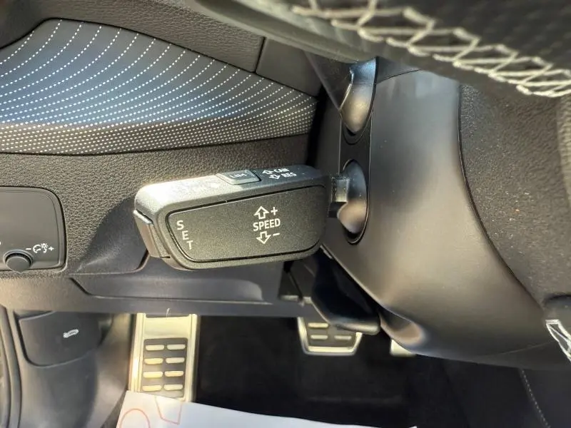 Gros plan sur la commande de régulateur de vitesse à gauche du volant dans l'Audi Q2 35 TDI S line 2025, intérieur noir.