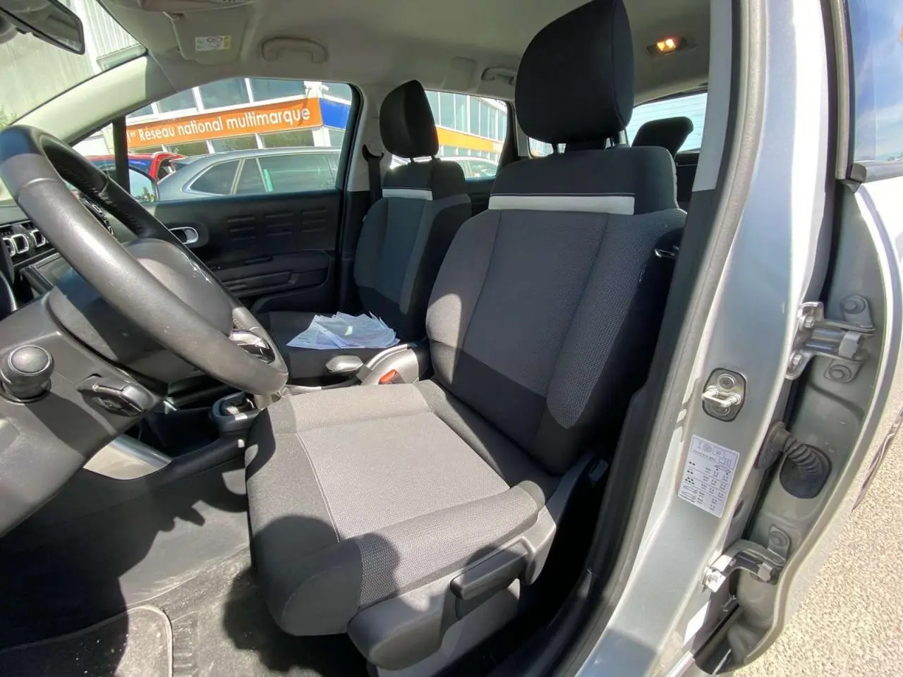 Vue intérieure côté conducteur du Citroën C3 Aircross gris Artense, montrant les sièges avant et le volant.