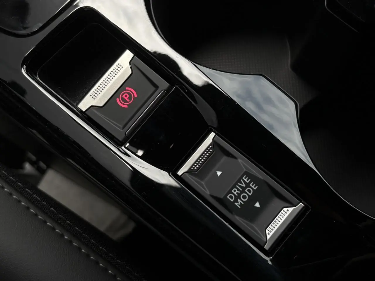 Gros plan sur la console centrale noire brillante de la Peugeot 208 Hybrid avec bouton frein électrique et sélecteur Drive Mode.