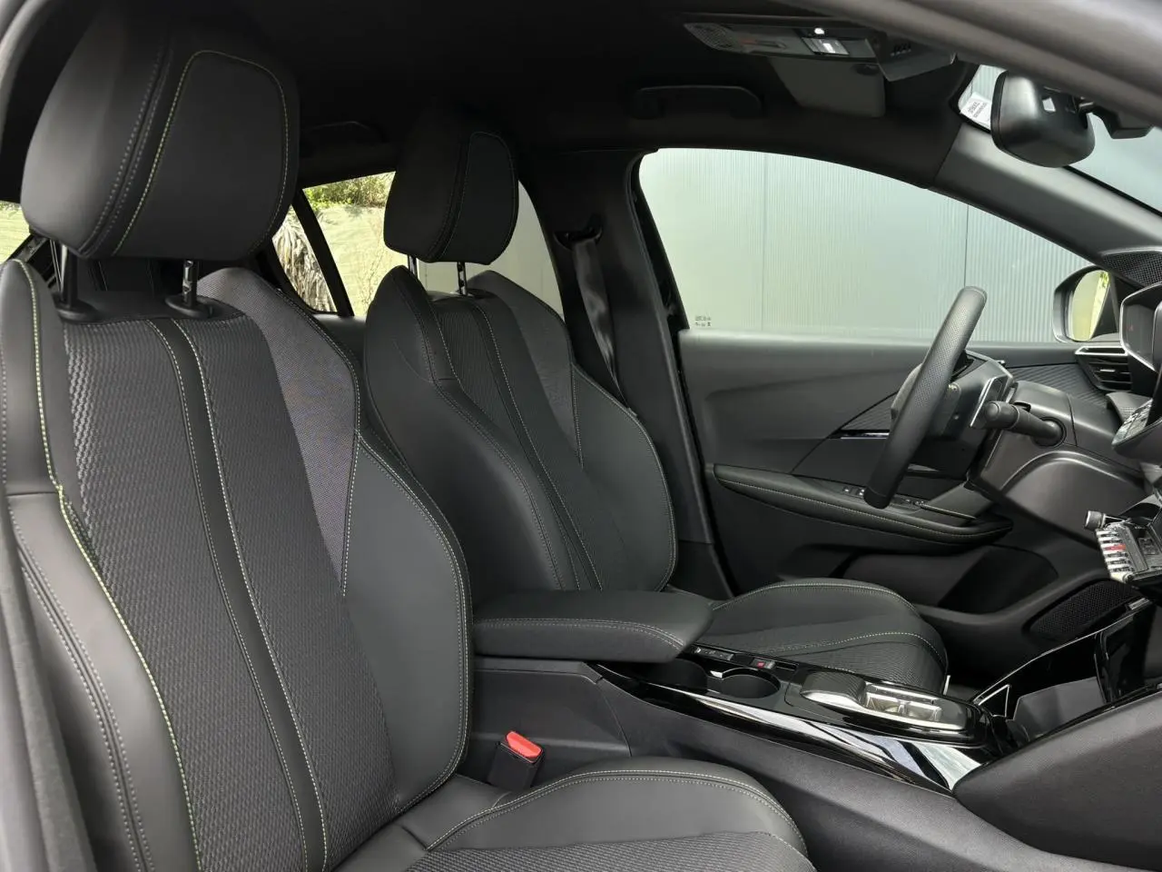 Vue intérieure côté conducteur de la Peugeot 208 Hybrid 110 e-DSC6 GT avec sellerie noire et surpiqûres vertes Adamite.