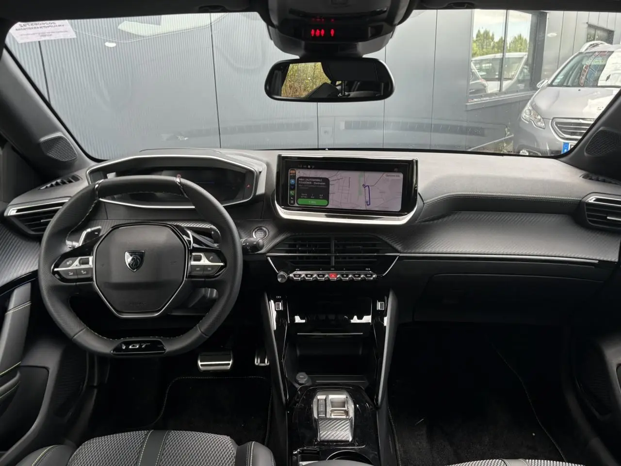 Vue intérieure avant du Peugeot 208 Hybrid GT 2025 avec tableau de bord noir, volant compact GT et écran tactile central.