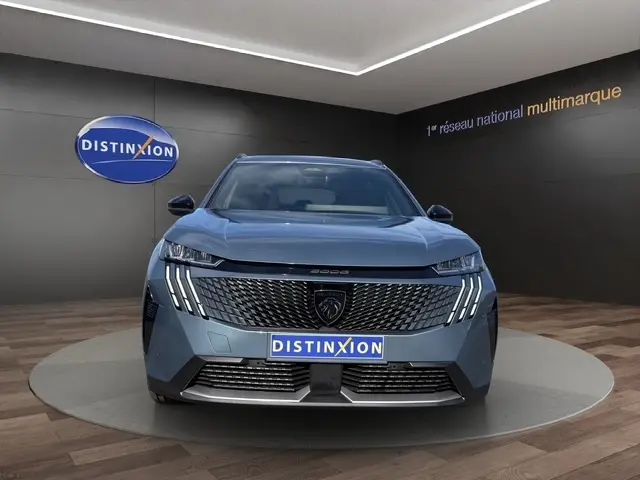 Vue frontale du Peugeot 5008 bleu 2025 avec calandre distinctive et feux LED en griffes, sur podium intérieur.