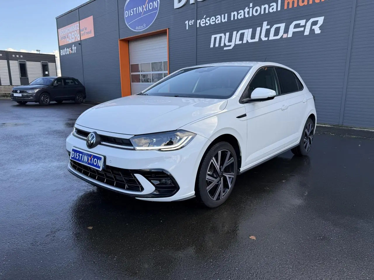 Volkswagen Polo blanc pur vue 3/4 avant droit avec jantes alliage et calandre R-Line devant un bâtiment gris.
