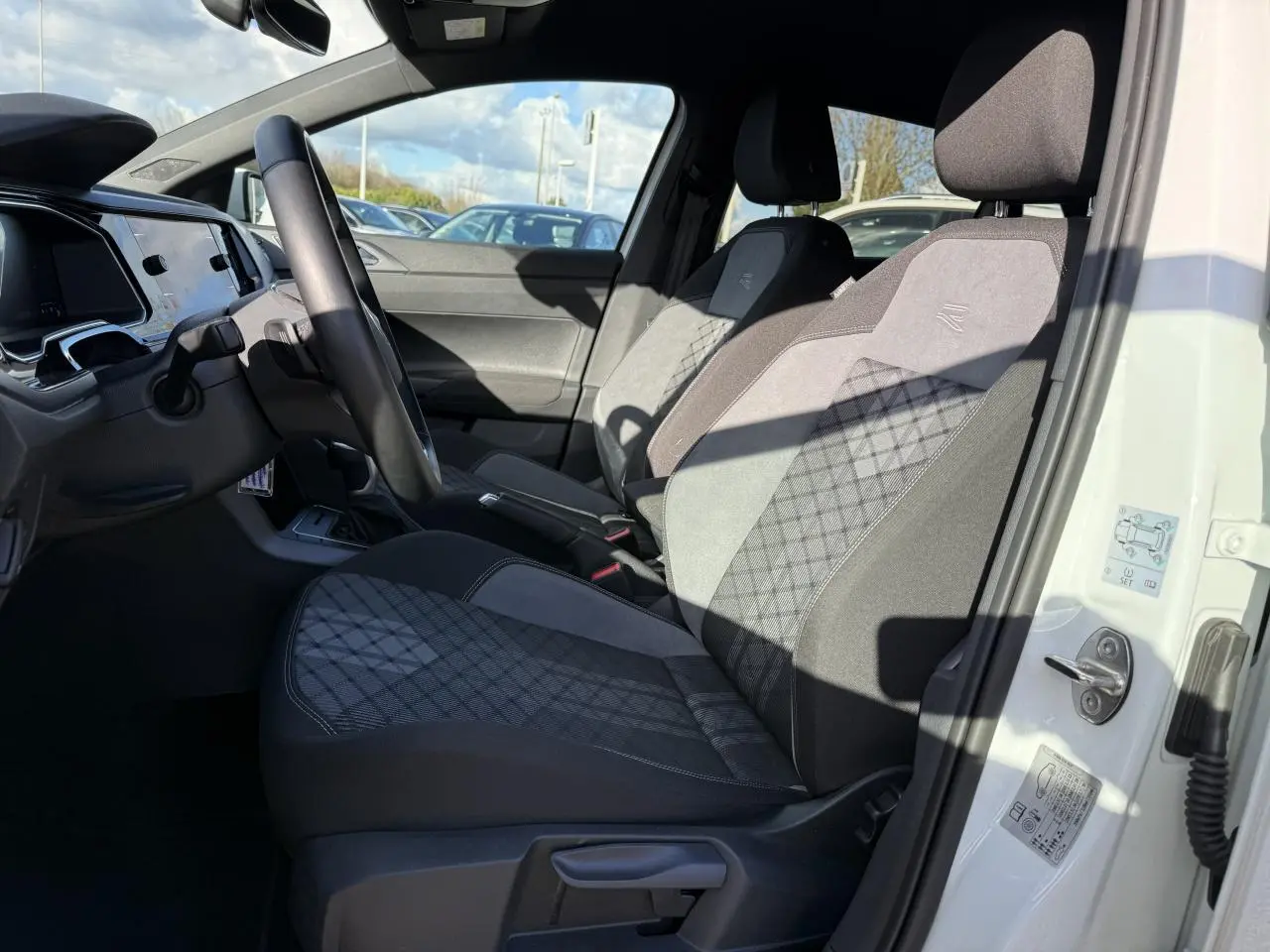 Intérieur côté conducteur d'une Volkswagen Polo blanc pur 2025, sièges R-Line en tissu gris avec motifs losanges.