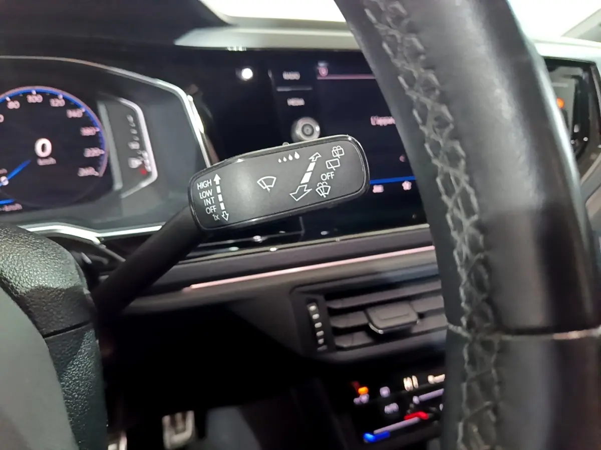 Gros plan sur le commodo d’essuie-glace dans l’habitacle noir du Volkswagen Taigo blanc, tableau de bord numérique en arrière-plan.