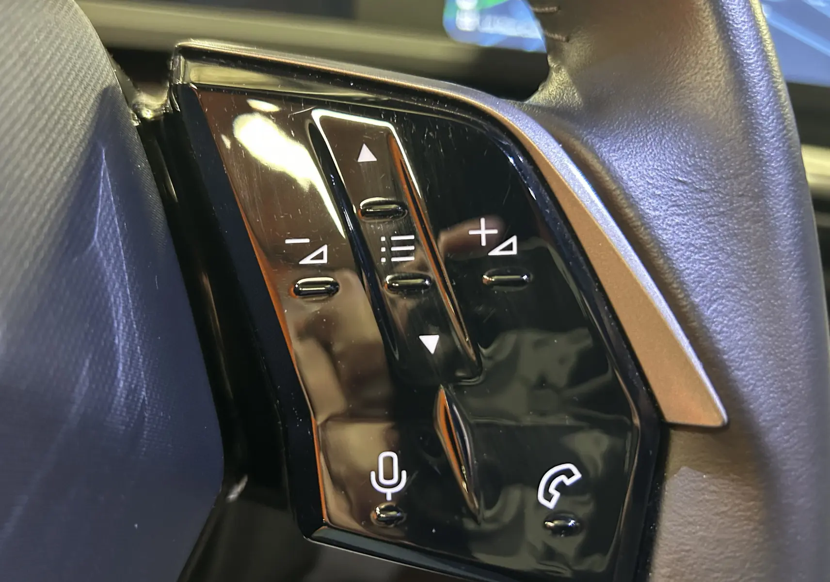 Gros plan sur les commandes au volant noir du Peugeot 5008 hybride 2025, avec boutons de volume et téléphone.