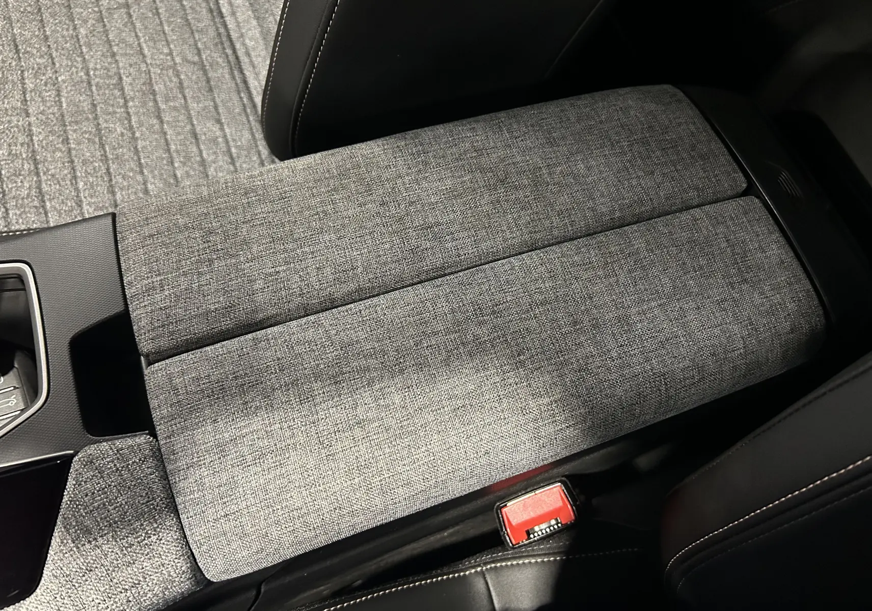 Gros plan sur l'accoudoir central en tissu gris à motifs, intérieur du Peugeot 5008 III Hybrid 2025.