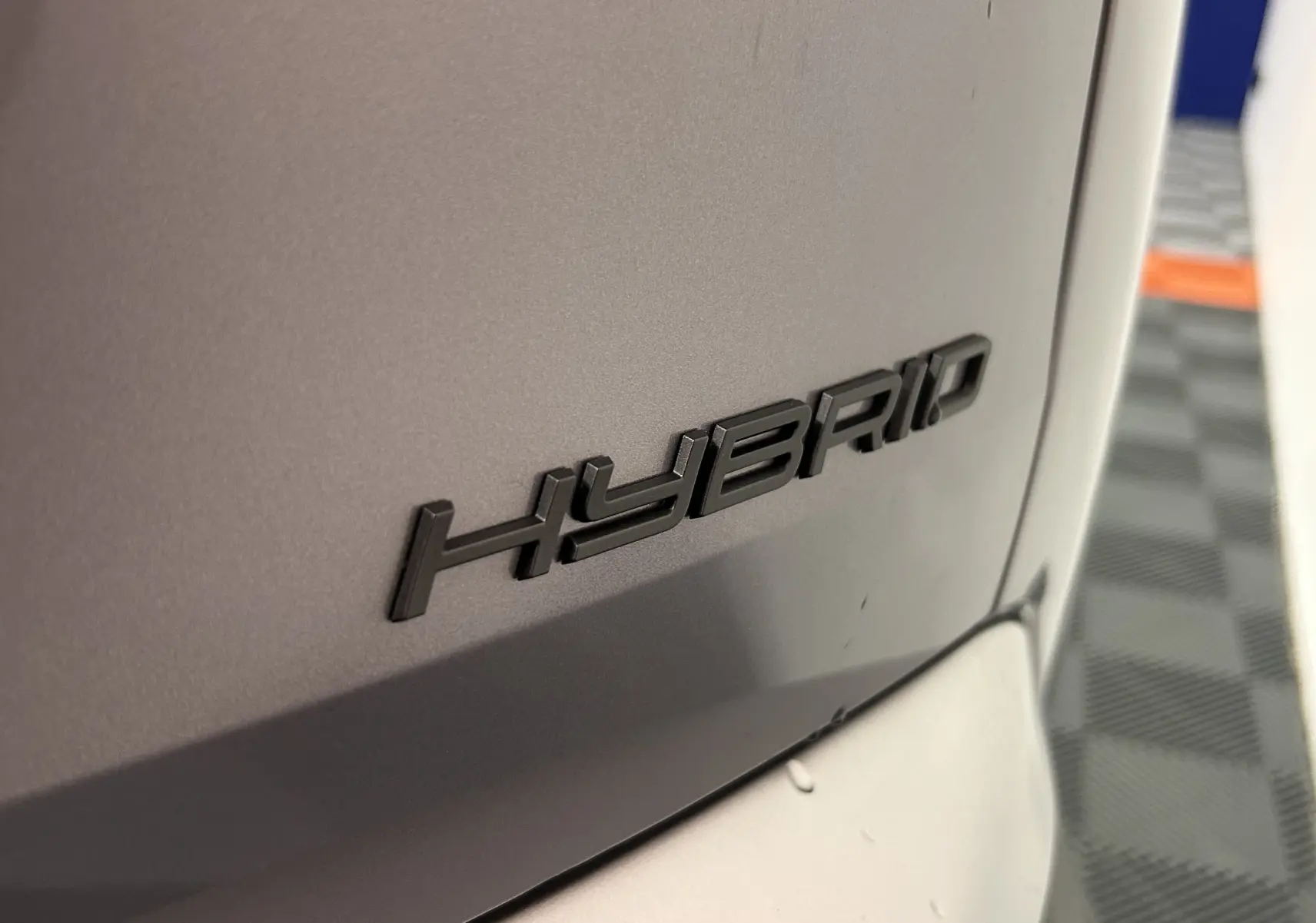 Gros plan sur l’inscription HYBRID en relief sur la carrosserie gris Artense du Peugeot 5008 III Hybrid 145.