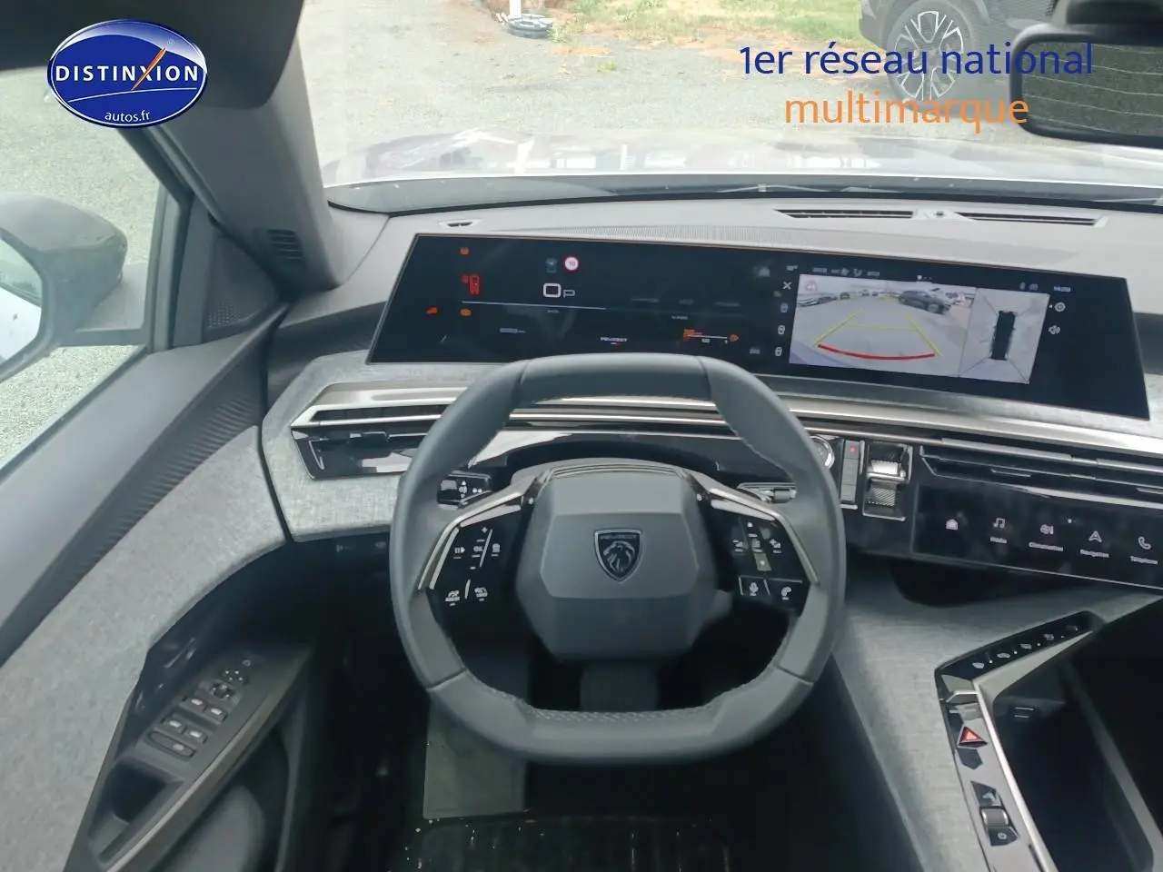 Vue intérieure centrée sur le volant Peugeot 5008 gris Artense avec tableau de bord numérique et caméra de recul affichée.