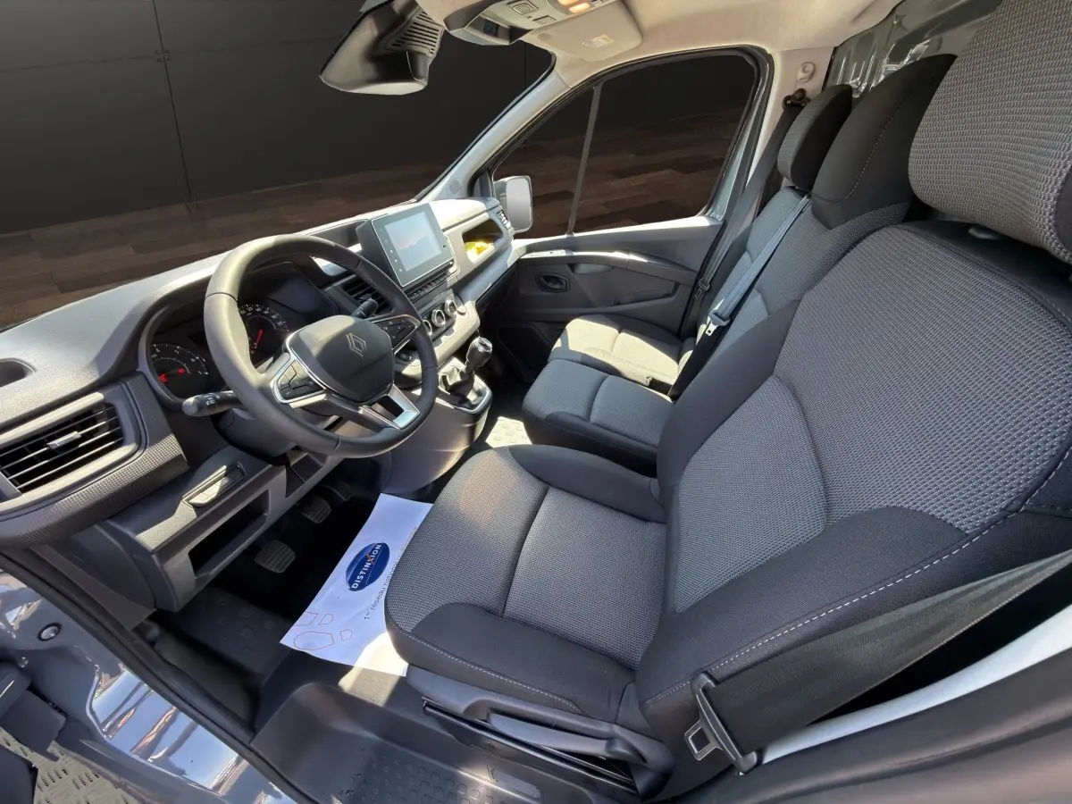 Vue intérieure côté conducteur du Renault Trafic Fourgon gris foncé, montrant le volant multifonctions et les sièges tissu gris.