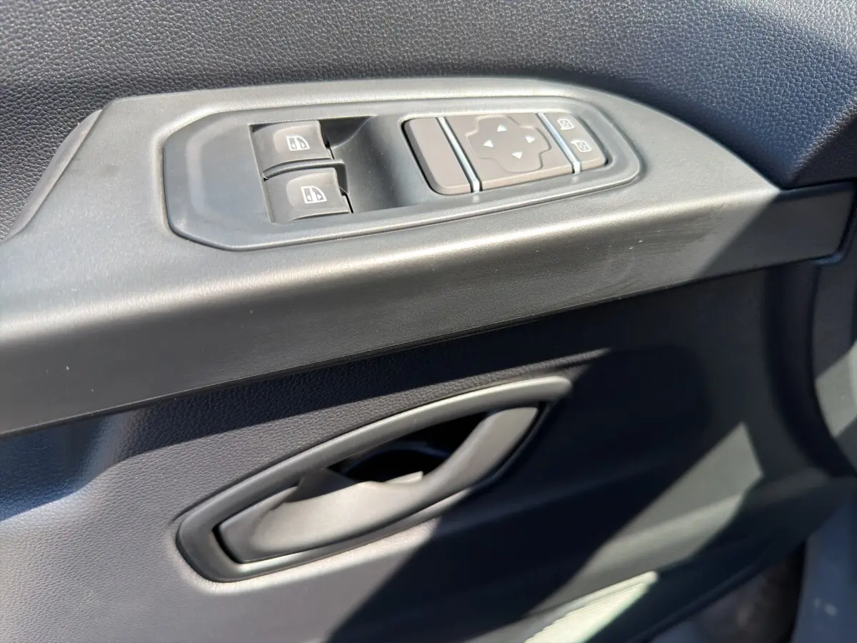 Gros plan sur la commande des vitres électriques et réglage des rétroviseurs côté conducteur du Renault Trafic Fourgon gris foncé.