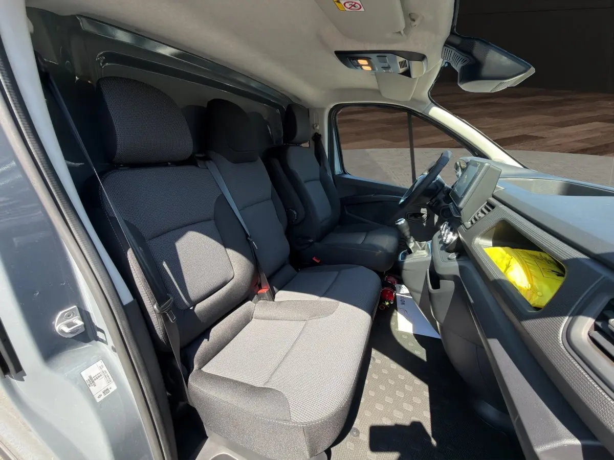 Intérieur du Renault Trafic Fourgon gris foncé, vue côté conducteur montrant les sièges avant et le tableau de bord.