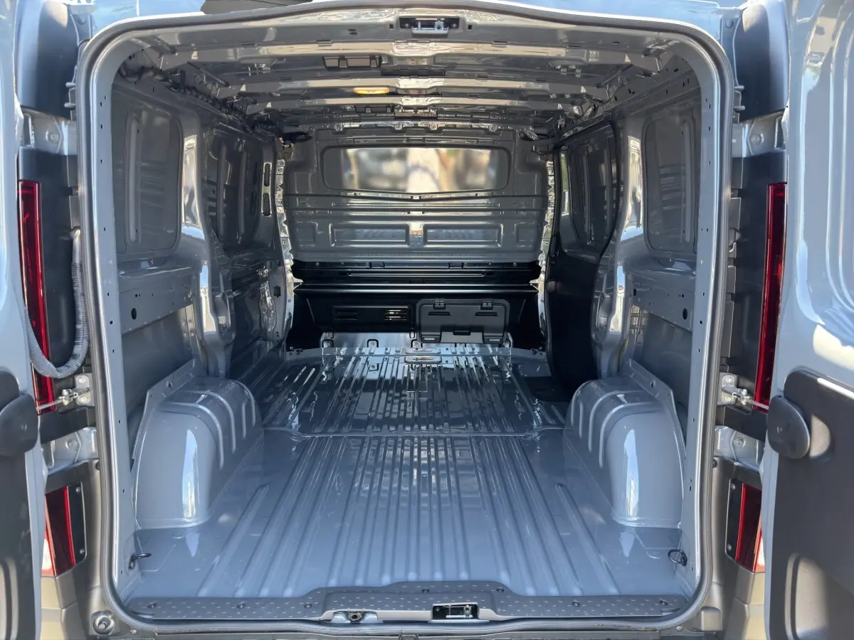 Vue intérieure arrière du fourgon Renault Trafic L1H1 gris foncé, montrant l'espace de chargement vide et la cloison pleine.