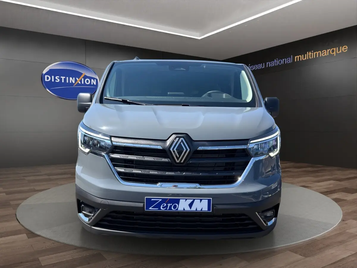 Vue avant d'un Renault Trafic Fourgon gris foncé avec calandre noire et phares LED allumés en showroom.