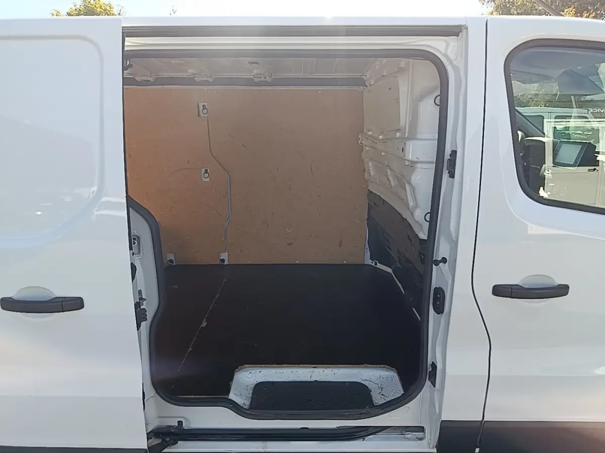 Vue latérale droite sur l’ouverture de la porte coulissante d’un Renault Trafic Fourgon blanc, montrant l’espace de chargement vide.