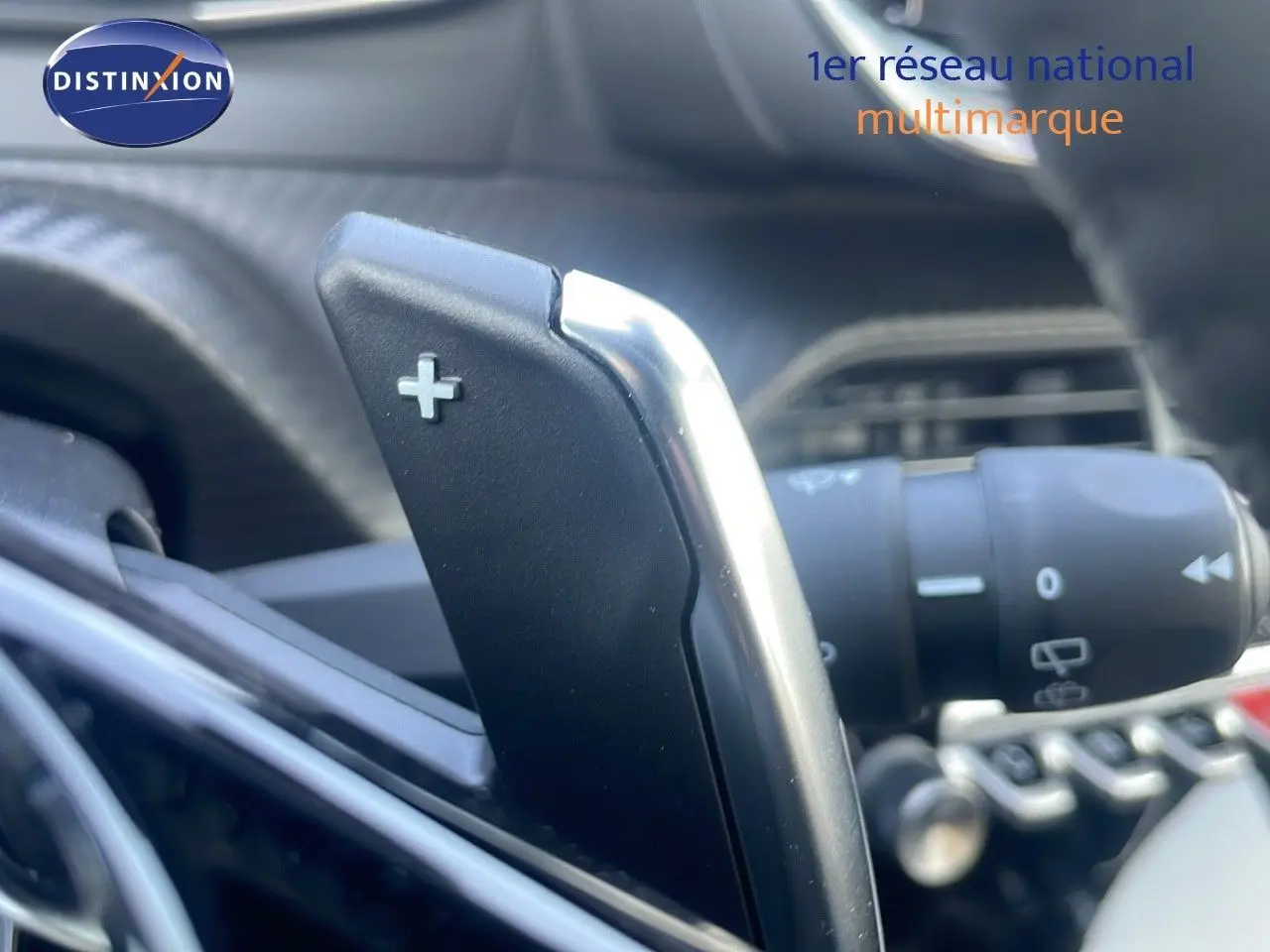 Gros plan sur la palette de changement de vitesse + au volant d'une Peugeot 2008 gris Artense, intérieur moderne.