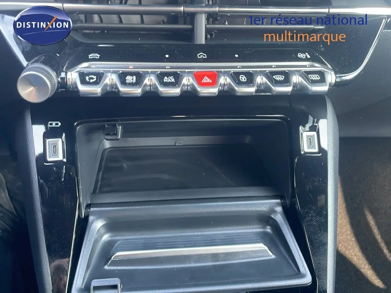 Gros plan sur la console centrale noire brillante du Peugeot 2008 Hybrid 136ch Allure avec boutons de commande et rangement ouvert.