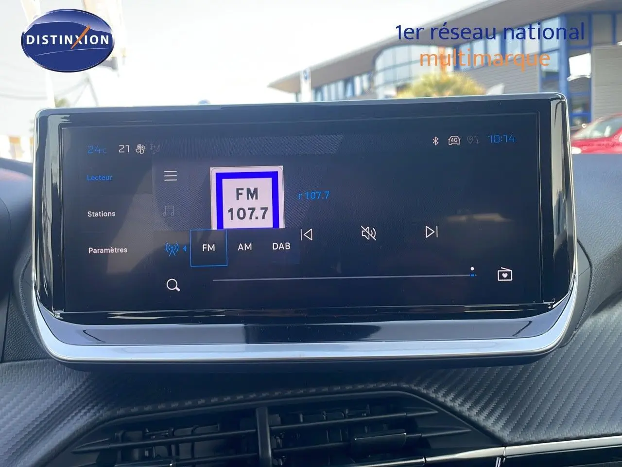 Écran tactile central du Peugeot 2008 Hybrid gris Artense, affichant la radio FM 107.7 en intérieur.