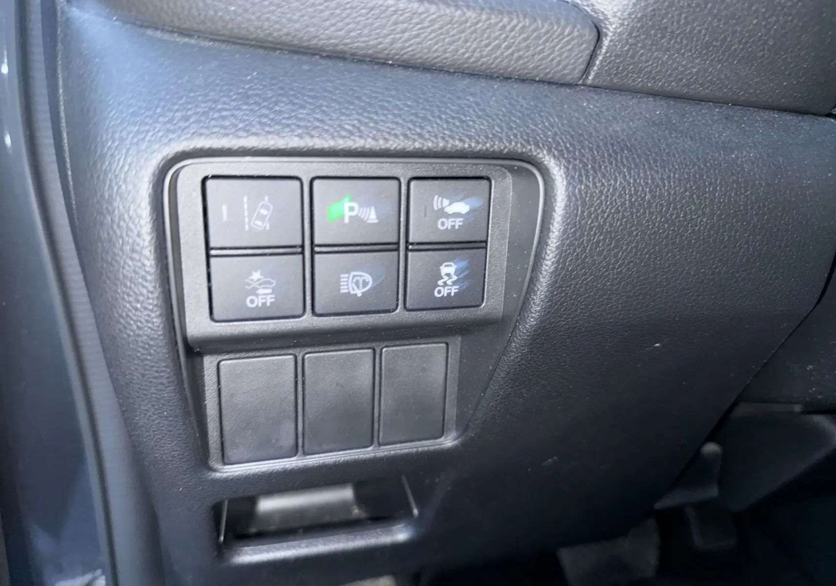 Gros plan sur les commandes noires du tableau de bord côté gauche du Honda CR-V Hybrid gris 2019, avec boutons d'assistance activés.