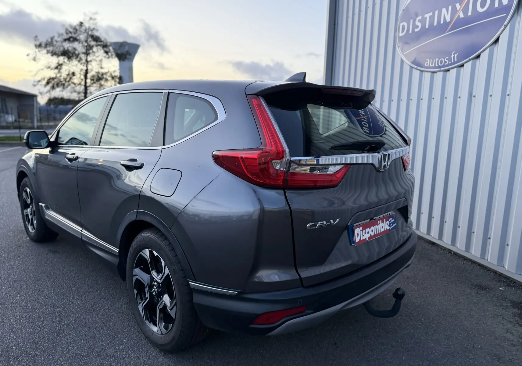 Vue 3/4 arrière droite d'un Honda CR-V gris 2019 avec feux arrière en forme de L et attelage visible.