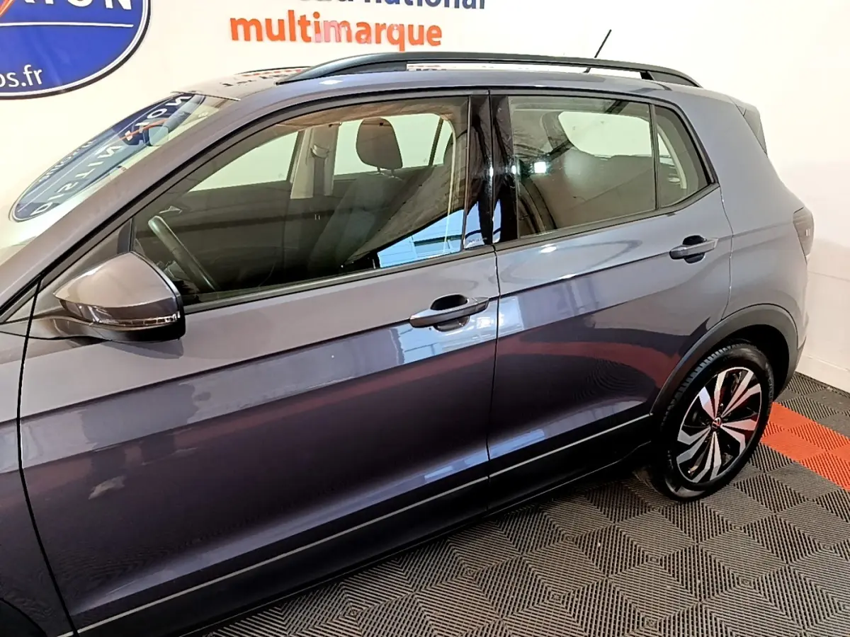 Vue de profil côté gauche du Volkswagen T-Cross gris foncé 2023 avec jantes alliage et barres de toit noires.