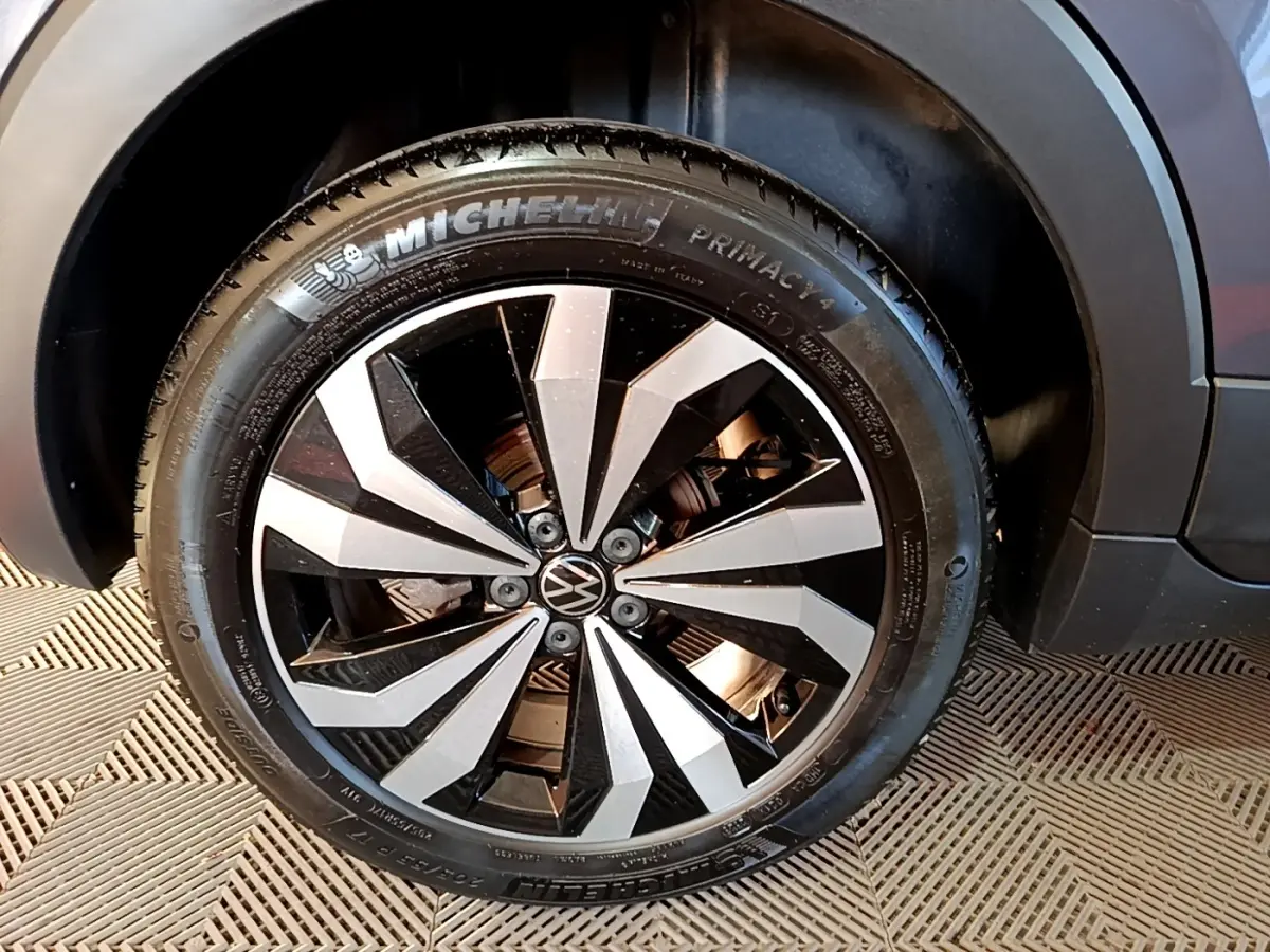 Gros plan sur la roue avant droite du Volkswagen T-Cross gris foncé, jante alliage bicolore au design géométrique.