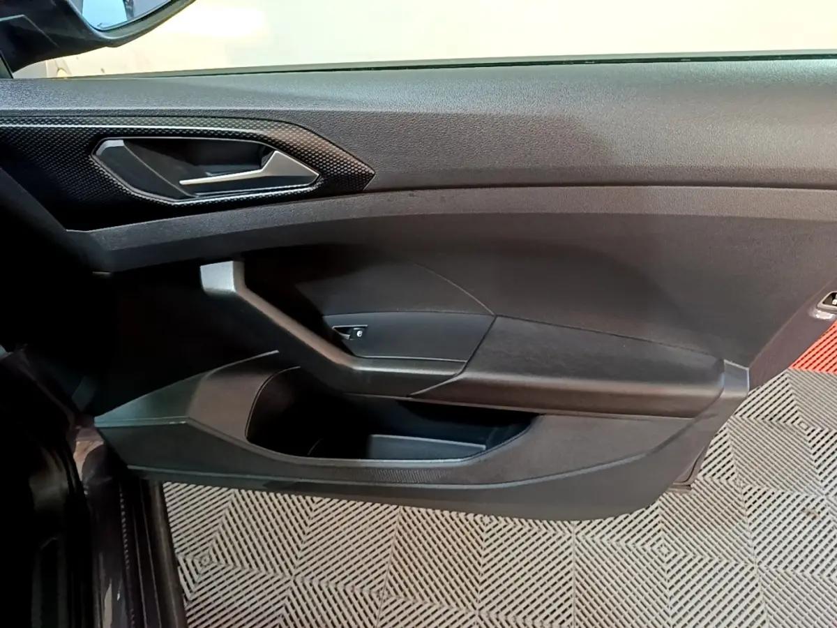 Vue intérieure côté gauche de la porte d’un Volkswagen T-Cross 2023 gris foncé avec poignée et rangement intégré.