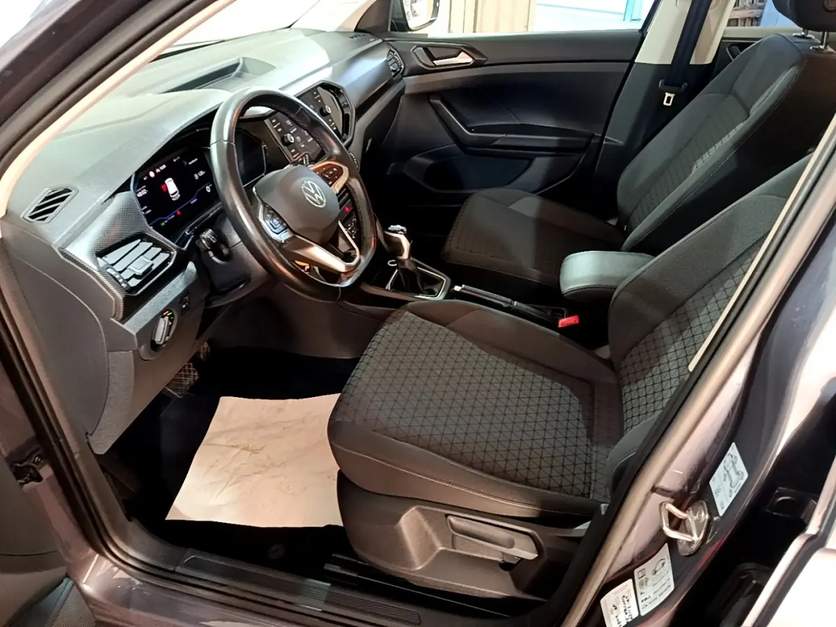 Vue intérieure côté conducteur du Volkswagen T-Cross gris foncé 2023, volant cuir multifonctions et sièges tissu noirs.