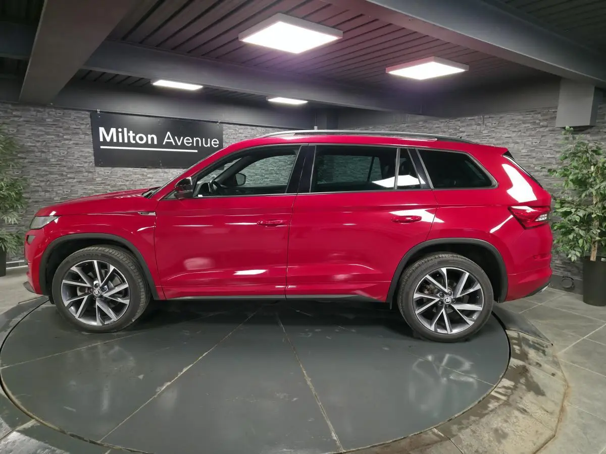 Vue latérale gauche d'un Skoda Kodiaq Sportline rouge métallisé avec jantes alliage 20 pouces dans un showroom intérieur.