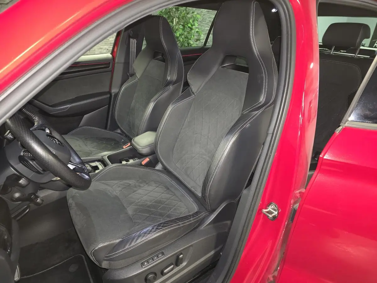 Vue intérieure côté conducteur d'un Skoda Kodiaq rouge 2021, sièges sport cuir/Alcantara noirs avec surpiqûres blanches.