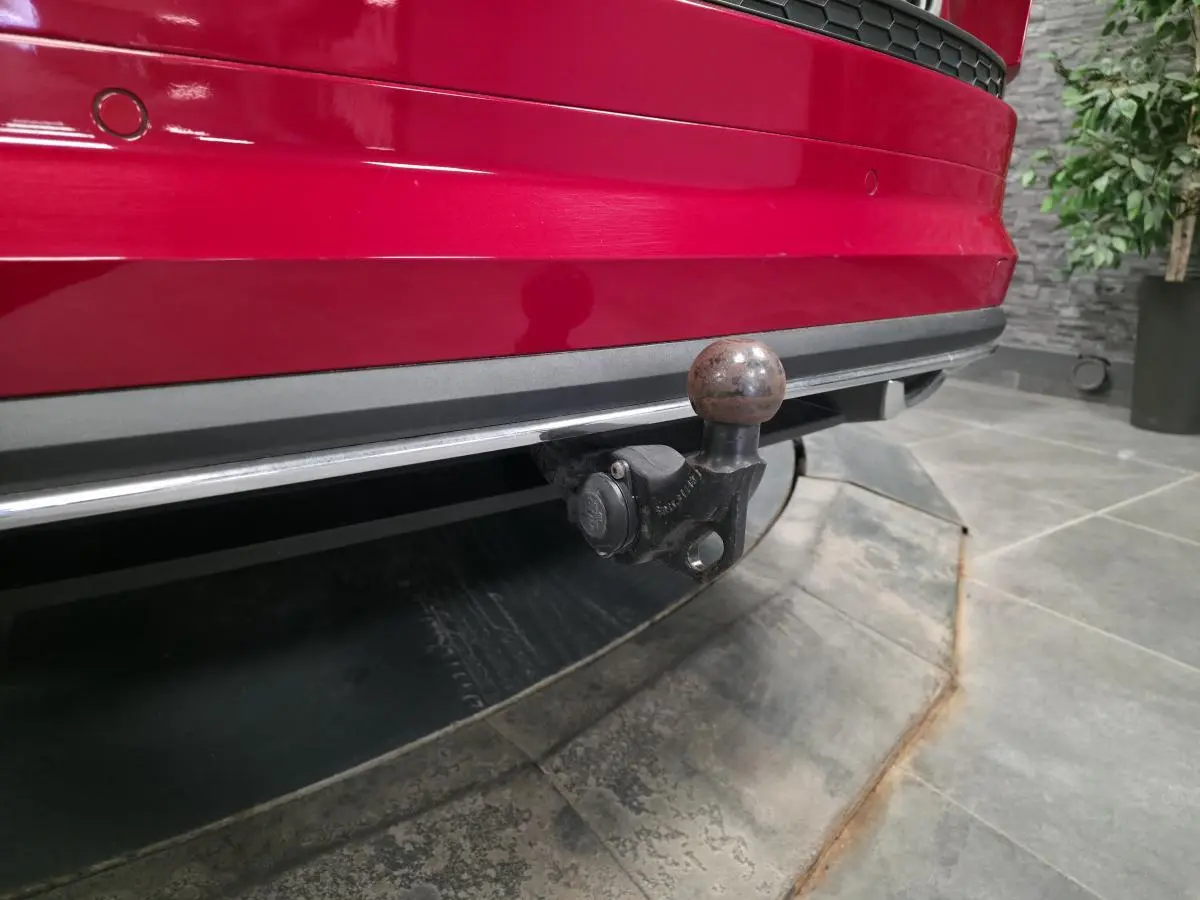 Gros plan sur le crochet d'attelage à l'arrière d'un Skoda Kodiaq rouge, avec pare-chocs et capteurs de stationnement visibles.